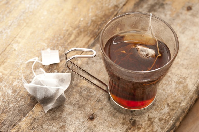 Cup of steeping black tea Cup of steeping black tea in a glass mug with a teabag in the boiling water and a second unused bag alongside on a beige background, high angle view