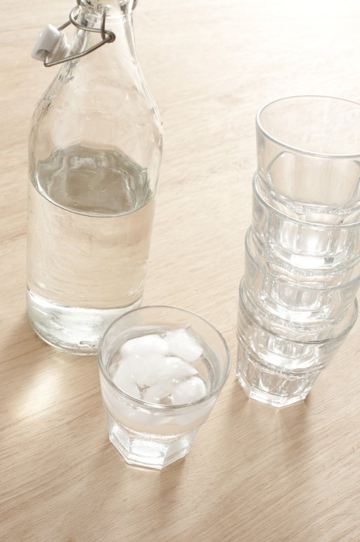 Glass bottle of pure fresh water Glass bottle of pure fresh water standing on a wooden table alongside a stack of tumblers and glass filled with liquid