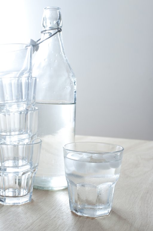 Refreshing cold pure water Refreshing cold pure water served in a glass bottle with one full tumbler and a stack of empty glasses alongside, healthy drink with copyspace
