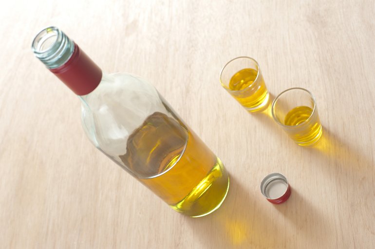 Bottle of alcoholic drink near two shot glasses Open bottle of alcoholic drink, whiskey, tequila or scotch, near two full shot glasses, on a wooden table, with copy space and shadow, high-angle
