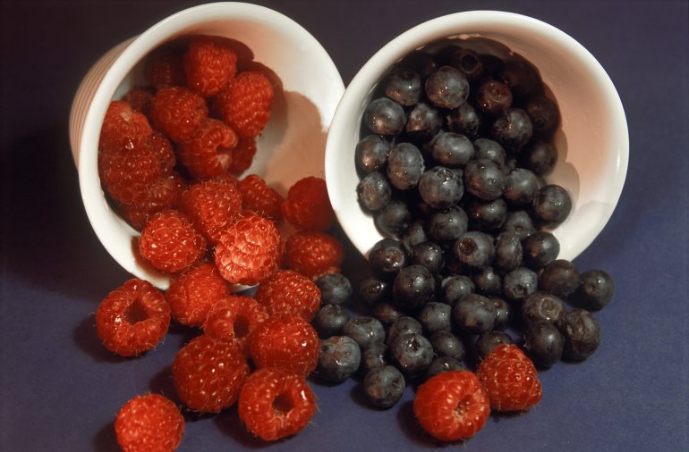 Autumn fruits - fresh ripe red raspberries and deep purple blackcurrants spilling from small ceramic containers, a healthy natural source of antioxidants