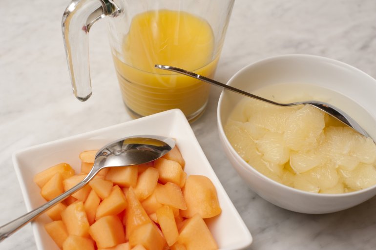 High Angle Close Up of Bowls of Fruit and Pitcher of Juice - Chunks of Melon and Pineapple in Dishes Beside Jug of Orange Juice