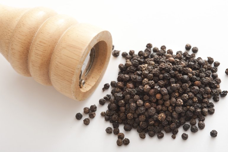 Pile of dried black peppercorns with mill Pile of dried black peppercorns with wooden pepper mill or grinder in a close up view on white