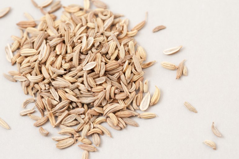 A pile of white caraway seeds on white background viewed in close-up from above