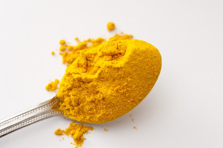 Silver teaspoon heaped with ground dried turmeric powder over a white background with copy space