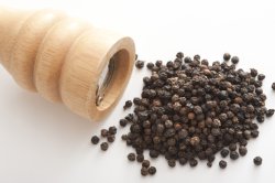 Pile of dried black peppercorns with mill