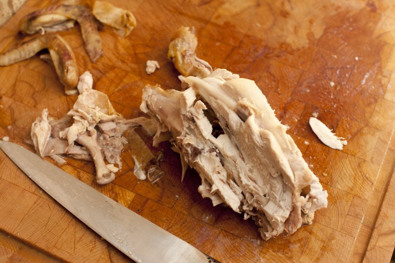 The carcass and left over remnants of a roast chicken on a wooden board with a carving knife, viewed from above