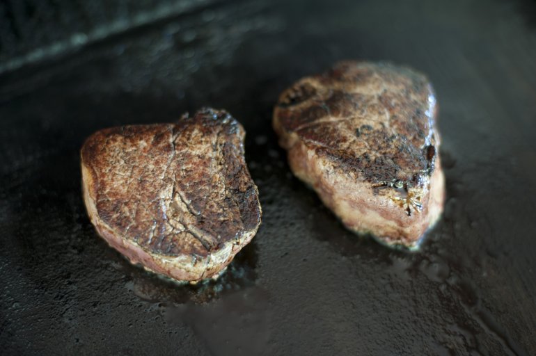 Cooking two medallions of fillet steak searing them on a hot griddle to seal in the flavour, close up high angle view