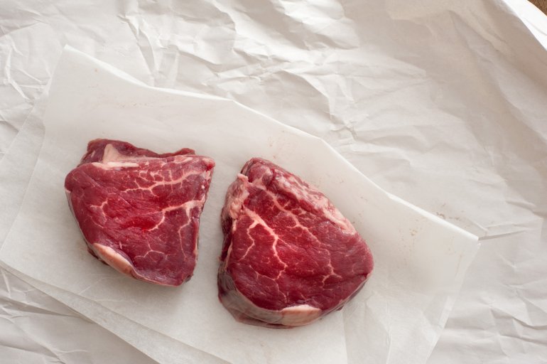 Two uncooked joints of beef lying on baking paper. From above