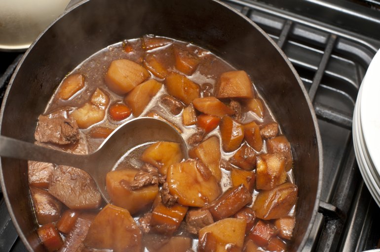 Delicious hot soup or stew with potatoes, meat, different vegetables in saucepan on stove. From above