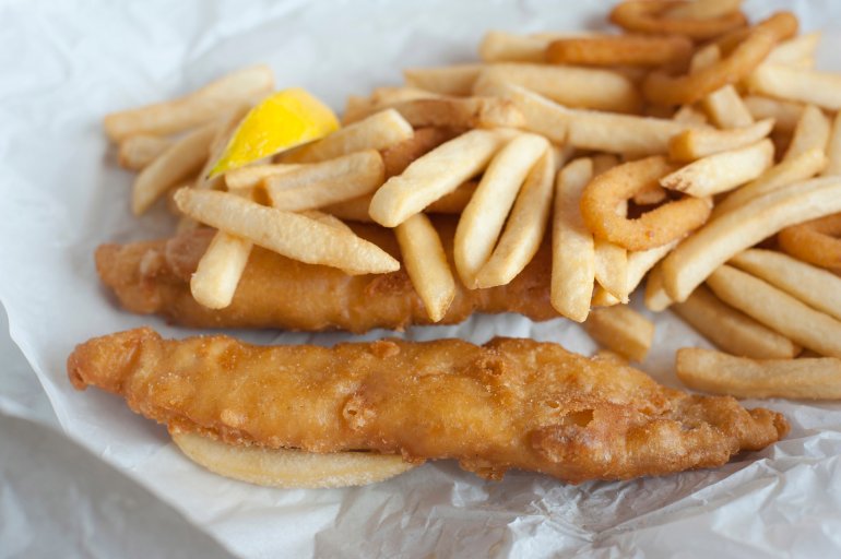Takeaway meal of battered fried fish and potato chips on a crumpled sheet of greaseproof paper