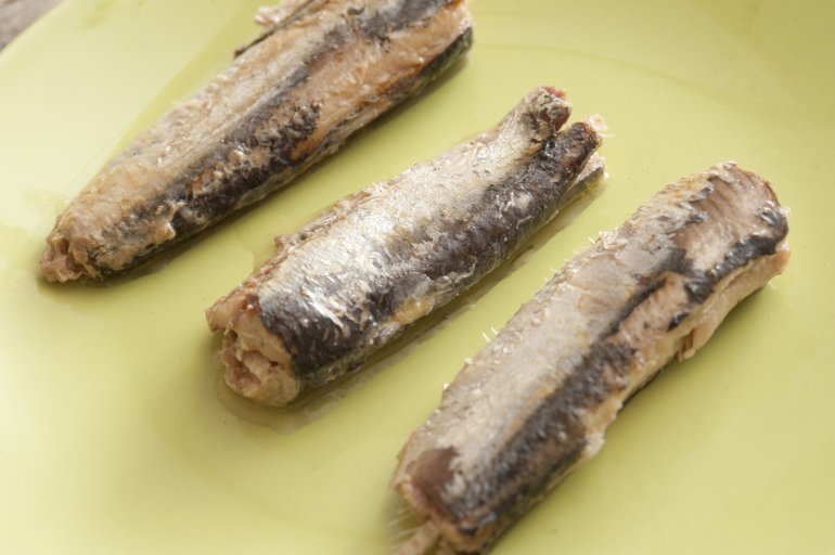 Three canned sardines on a yellow plate arranged separately in a neat row, close up high angle view