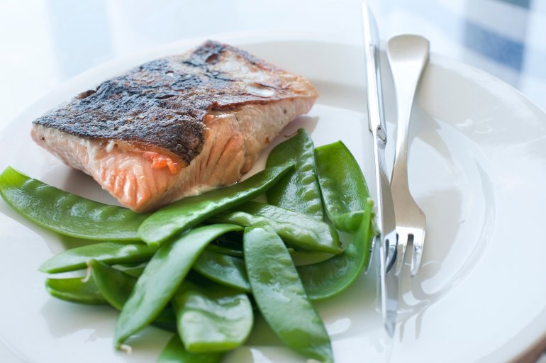 Cooked fresh salmon steak served with delicious sugersnap peas, closeup view with shallow dof