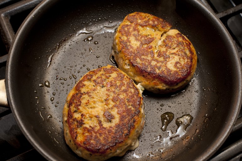 Pair of delicious cooked crab cakes frying in non-stick pan with drops of oil bubbling