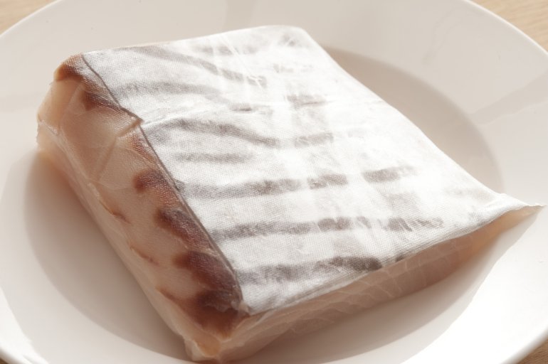 Single raw fillet of mackerel fish wrapped in wax paper on ivory colored round plate