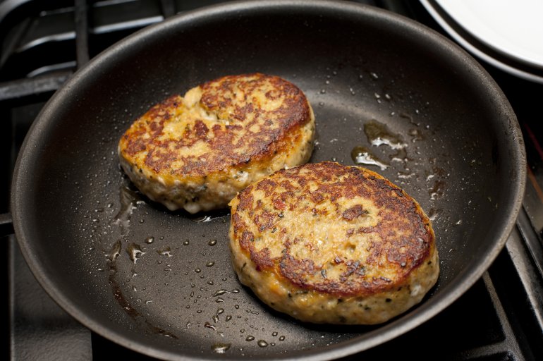 Close up on two round well cooked fried fish patties in non-stick pan with light coating of oil