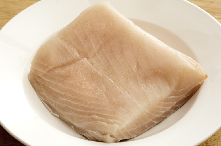 Top down close up view on single square shaped piece of raw mackerel meat in the middle of round white china plate