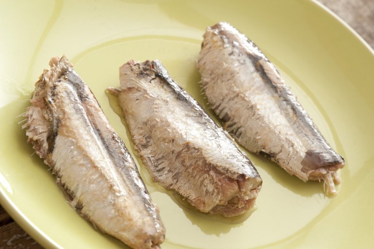 Close up on three ready to eat sardine pieces placed neatly as a row in center of glossy green plate