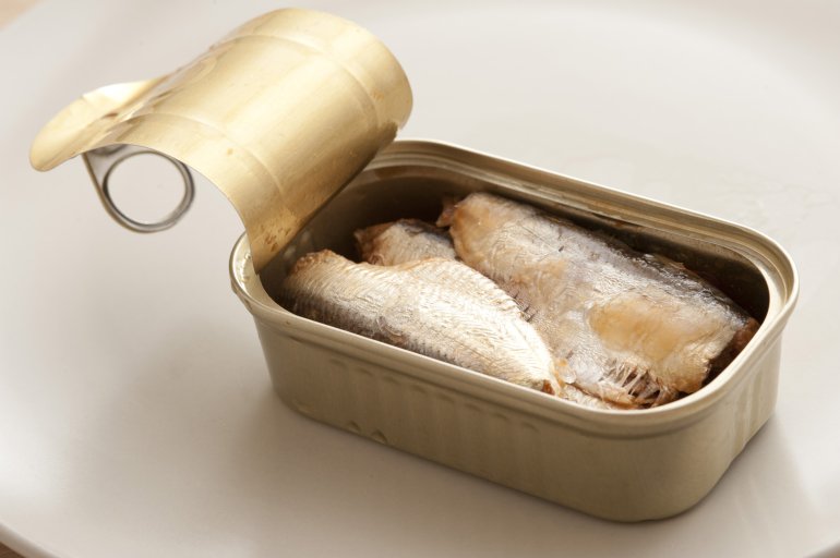Single open aluminum can of drained sardines ready to eat over white table background