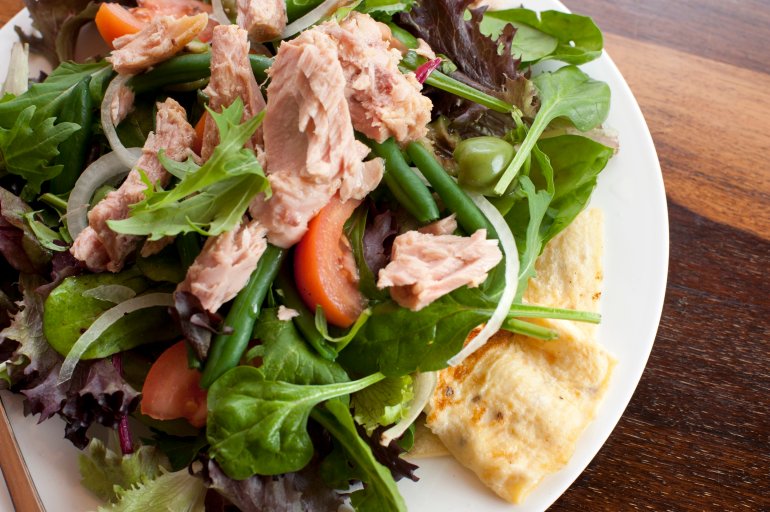 Tuna nicoise salad with fresh leafy greens and herbs served over an omelette, overhead close up view