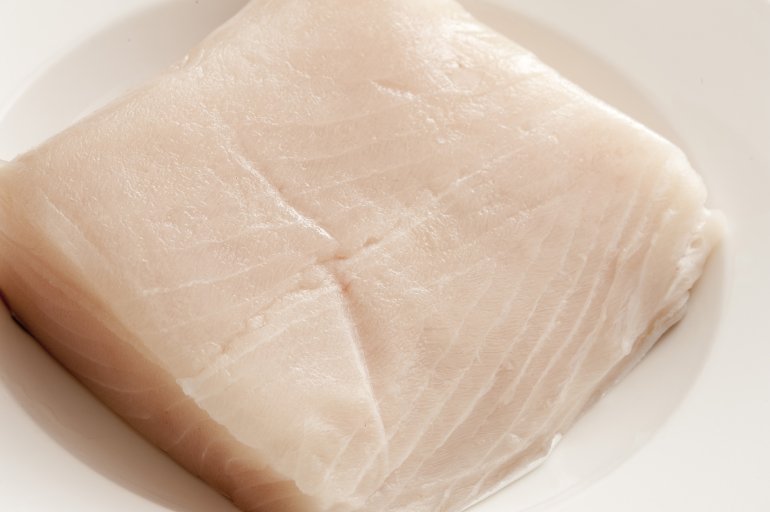 Close up on raw piece of light colored mackerel fish on white shiny plate