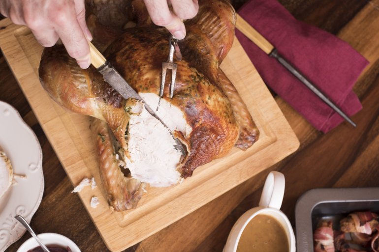 Man carving the breast of a Christmas turkey with vintage utensils in a cropped overhead view on the table