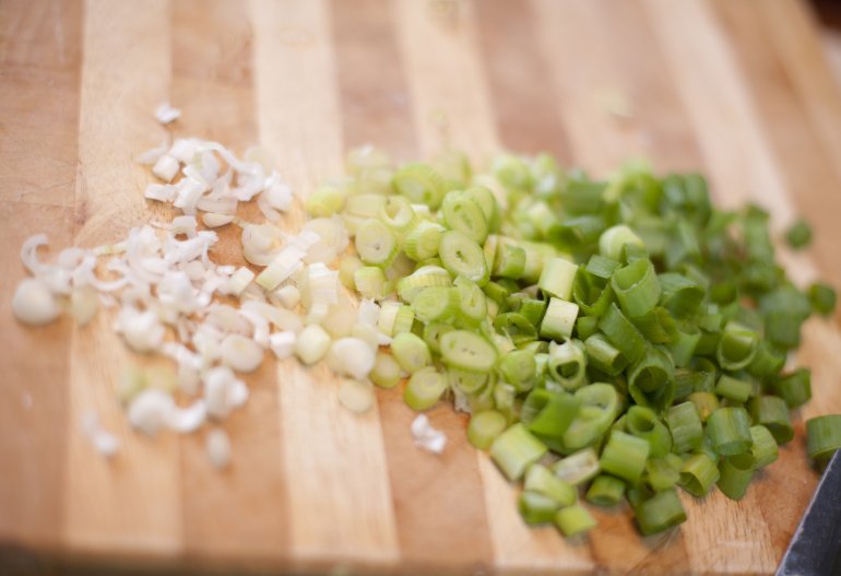 Chopped fresh spring onions into two heaps, green and white, on a wooden chopping board during preparation for use as a garnish or in salads