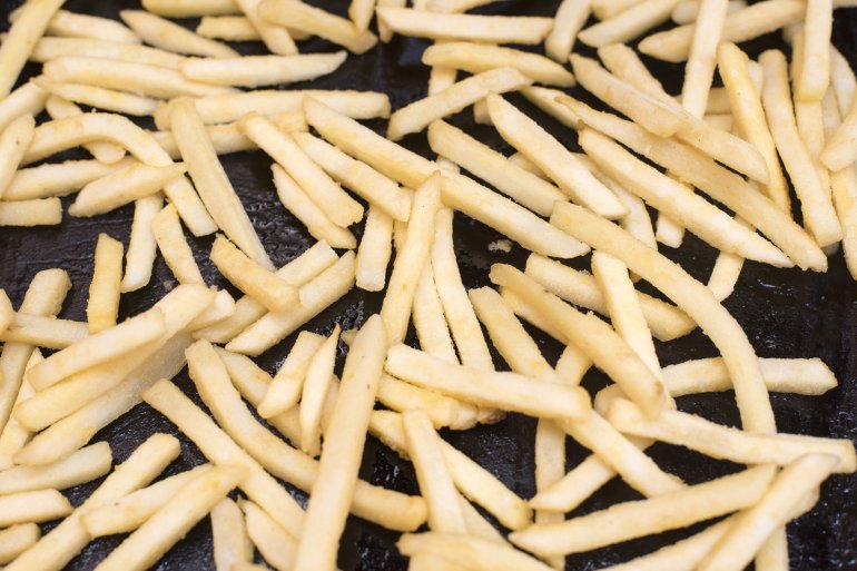 Fresh oven fries or potato chips spread on a tray for baking in a full frame background view