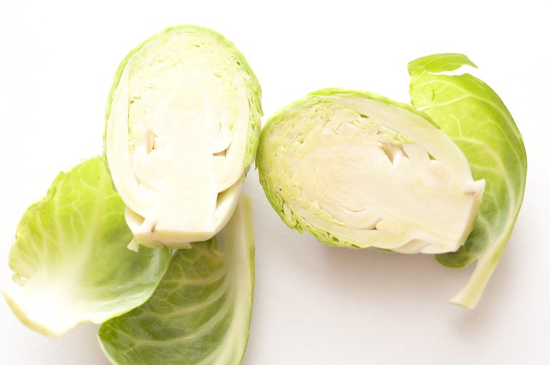 Raw Brussels sprouts head cut in half, viewed in close-up on white surface background
