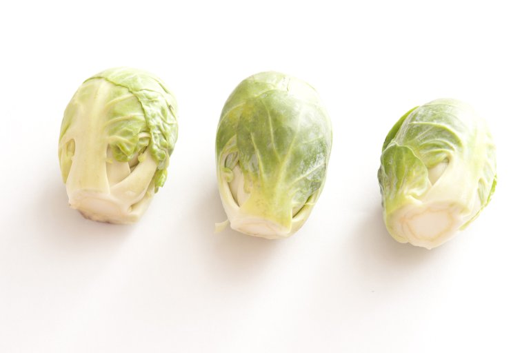 A close up of three brussel sprouts on a white background with copy space.