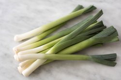 Several fresh, green leeks on a marble bench top